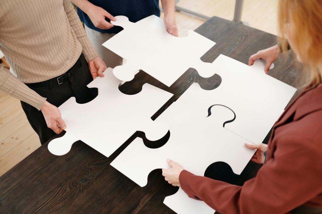 pexels photo 6147365 6147365 Four people collaborate by assembling large white puzzle pieces on a table.